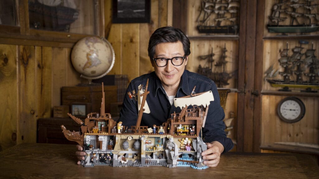 Ke Huy Quan sits with LEGO Ideas The Goonies ship set