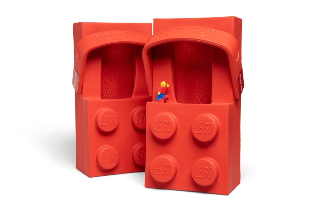 A LEGO minifigure stands on a pair of human sized LEGO Crocs